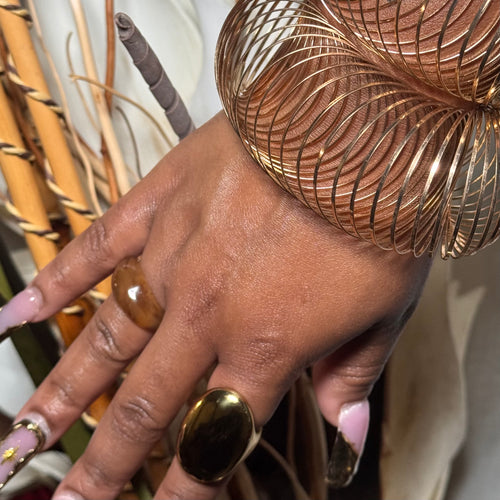 Hand with gold ring and bracelet against a blurred natural background