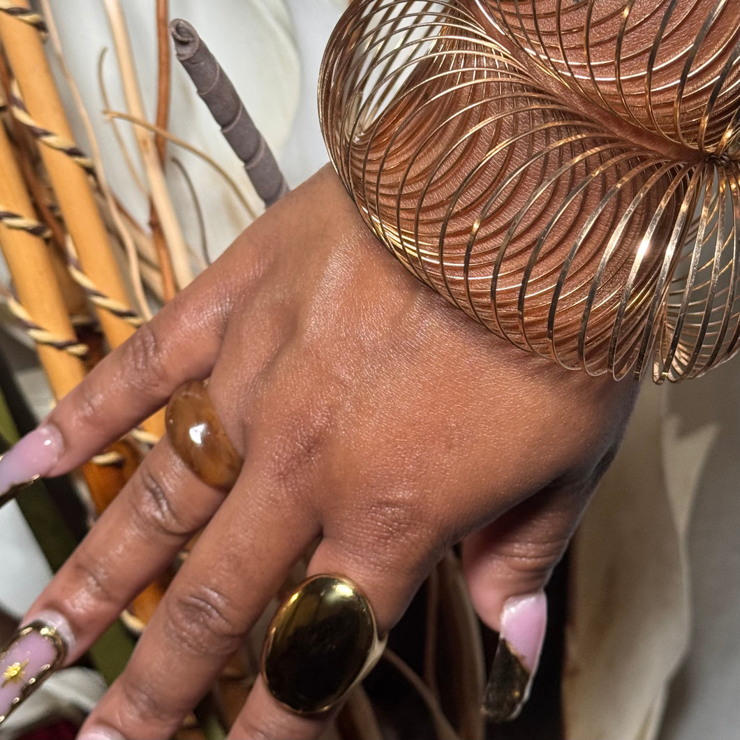 Hand with gold ring and bracelet against a blurred natural background