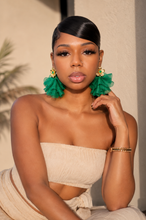 Load image into Gallery viewer, A woman with slicked-back black hair wearing large, vibrant green ruffled drop earrings with gold floral accents, paired with a beige strapless top and matching bottoms.
